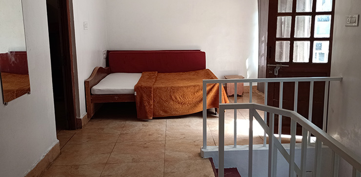 Room with a bed, orange blanket, mirror, and a wooden door near a staircase.