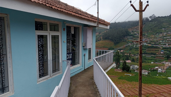 Blue hillside cottage with white-framed windows, a tiled roof, and a scenic valley view