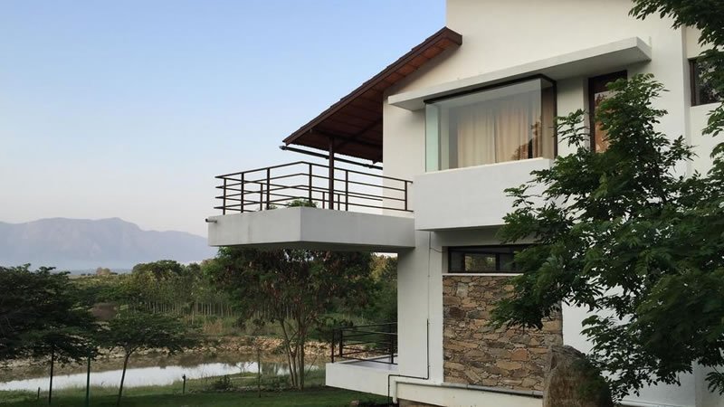 Modern holiday home with covered balcony overlooking trees, hills and a small lake