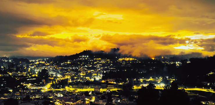Evening view of Ooty with town lights and glowing sky, seen from a cottage.