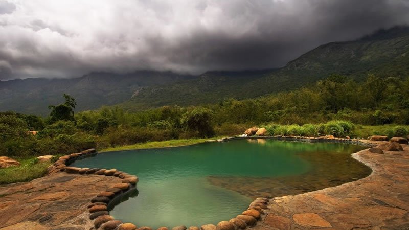 Outdoor natural pool overlooking green mountains beneath dramatic cloudy skies