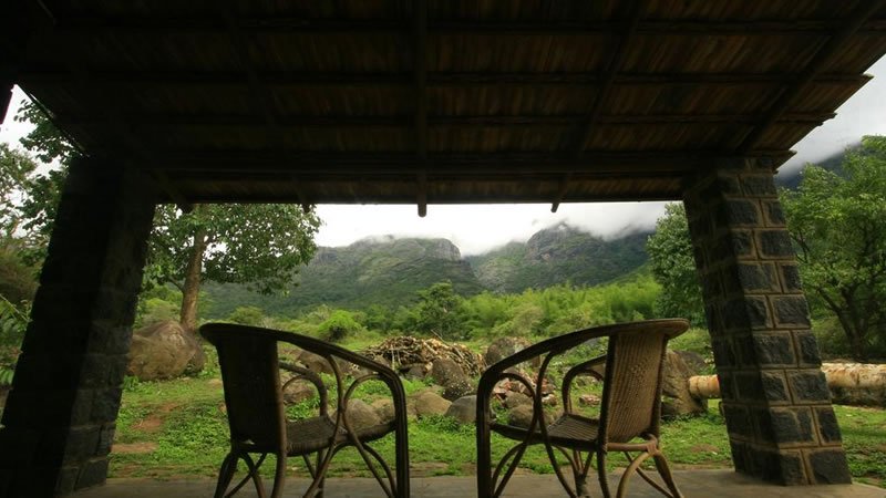 Covered veranda with chairs overlooking lush green mountains and misty hills