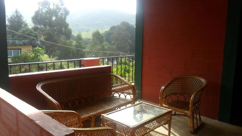 Covered balcony with wicker seating overlooking trees and green hills