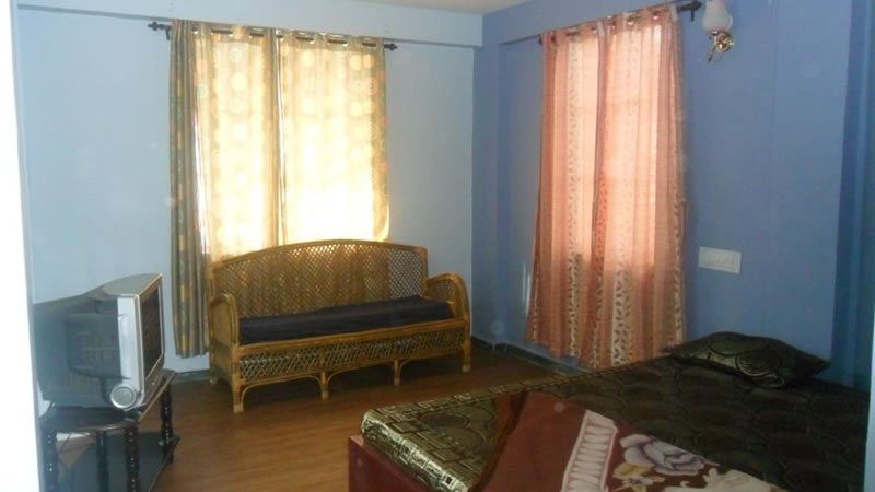 Bedroom with bed, wicker sofa, television and large curtained window