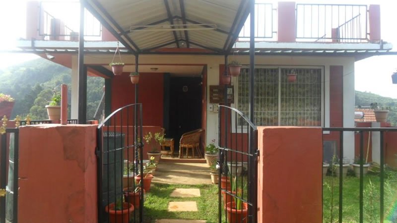 Holiday home entrance with covered porch, garden pathway, potted plants and metal gate