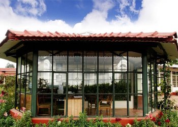 Glass-enclosed dining area at Sherlock Resort overlooking a lush garden and outdoor seating