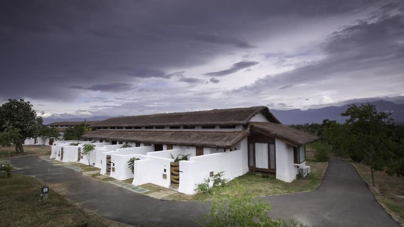 Row of white cottages with thatched roofs and mountain views under cloudy sky