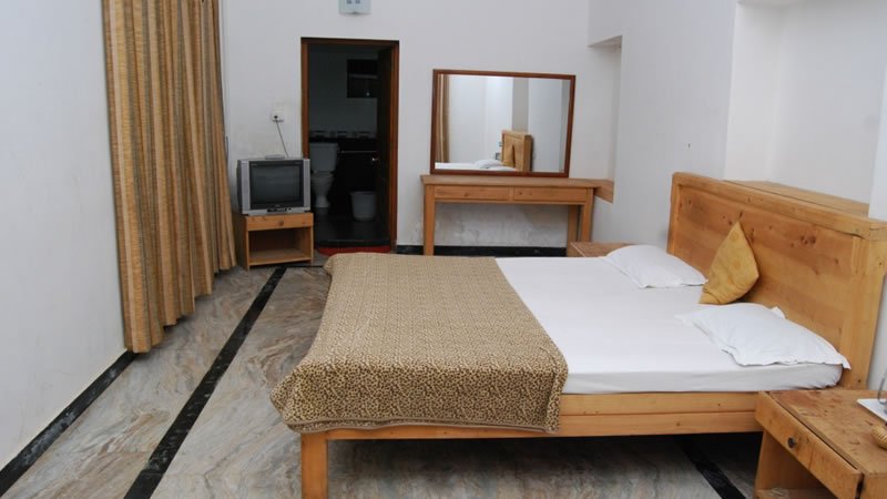 Spacious bedroom with wooden bed, dressing table, television and attached bathroom