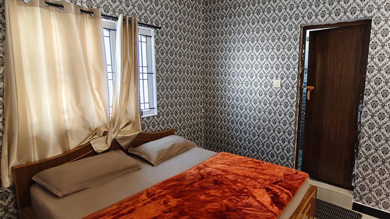 Bedroom with double bed, red blanket, patterned wall and attached bathroom door
