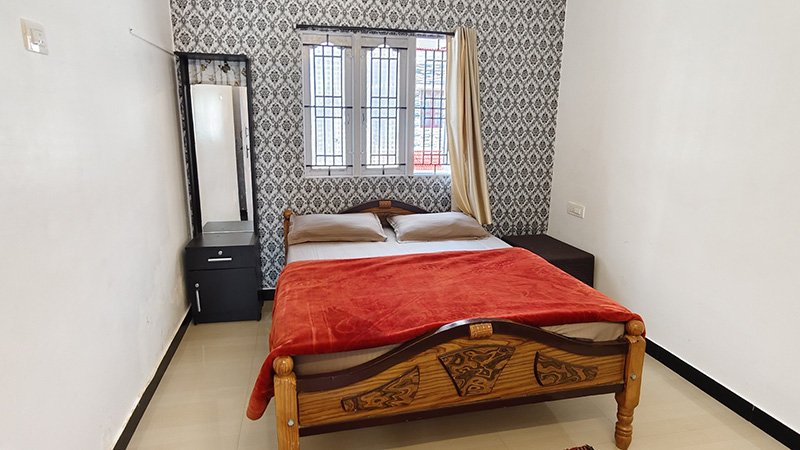 Bedroom with wooden double bed, red blanket, side table and window