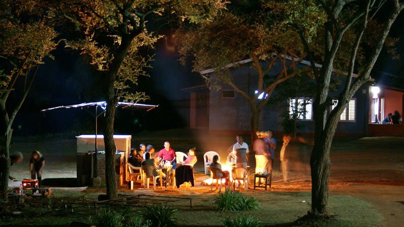 Guests gathered around an outdoor campfire beneath trees at night