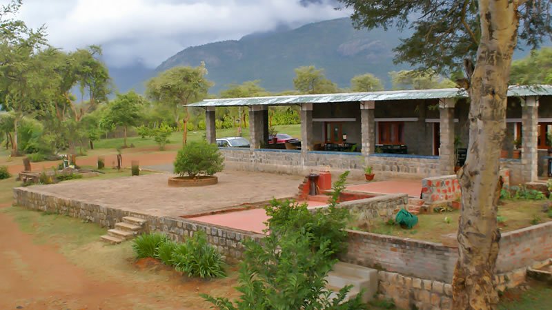 Stone building with open veranda surrounded by trees and mountain scenery