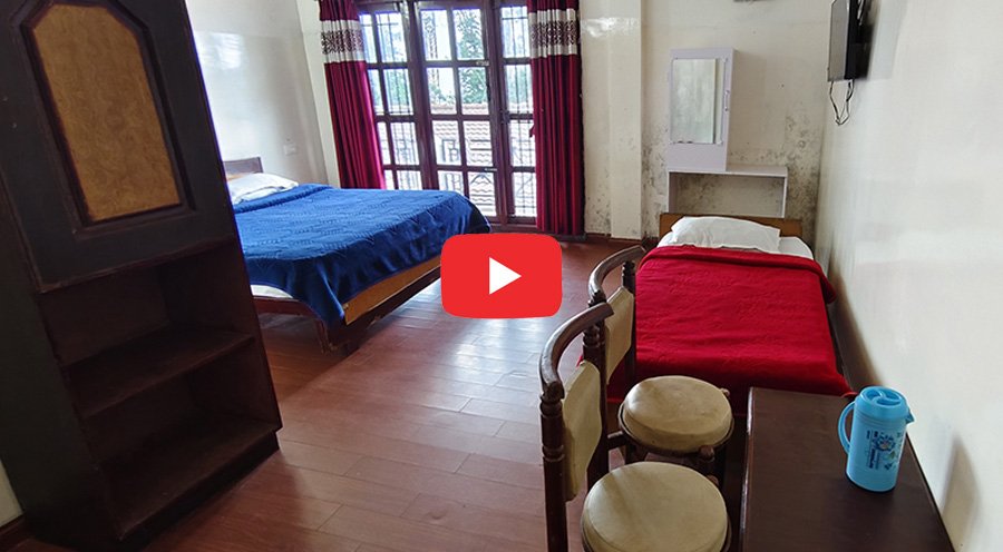 Simple hotel room with two beds, wooden floor, and large window.